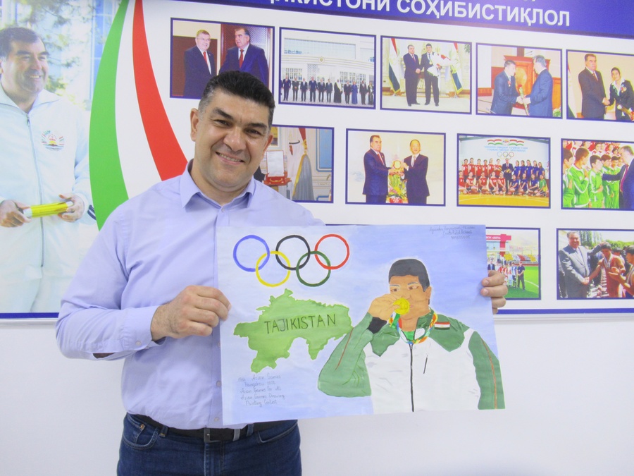 Tajikistan’s Rio 2016 champion Dilshod Nazarov holds up one of the entries in the Asian Games children’s art competition celebrating his golden achievement. © OCA